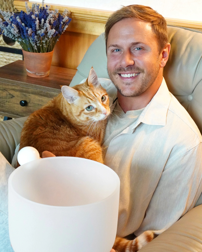 Man sitting on a couch with an orange cat, smiling at the camera.